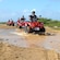 A group of people ride ATVs across a puddle and a dirt road